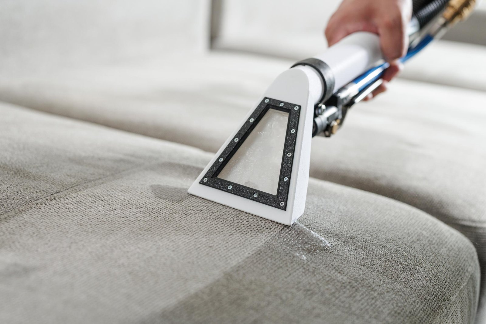 Fabric sofa being vacuumed to remove dust and debris before winter.